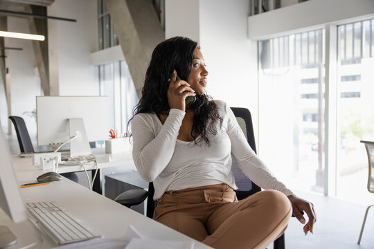 Businesswoman talking on smart phone, looking away at office desk