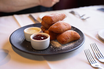 Beignets with powder sugar served with coffee creme anglaise and jam on a small black plate