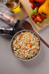 Couscous with vegetables in a rustic bowl surrounded by tomatoes, peppers and a glass of olive oil. Moroccan couscous. Top view.