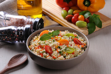 Couscous with vegetables in a rustic bowl surrounded by tomatoes, peppers and a glass of olive oil. Moroccan couscous. Selective focus.