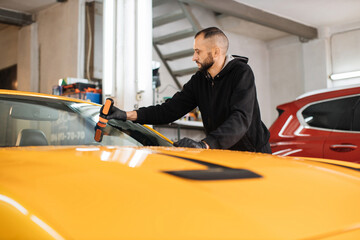 Attractive young bearded man in protective glove, applying anti-rain composition for yellow sport...