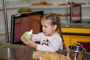 A little girl is sitting at the cash register in a children's store, playing as a seller, the child is playing role-playing games.
