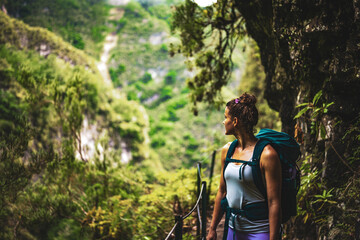 An athletic woman views into the distance from the adventurous jungle path along a green overgrown...