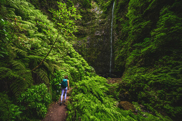 Beautiful athletic woman walks along flowery and farny trail at amazing jungle water fall. Levada of Caldeirão Verde, Madeira Island, Portugal, Europe.