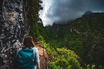 Beautiful woman admires the view from the adventurous cliff jungle path along the canal. Levada of...