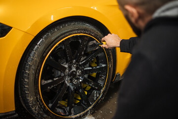 Close up of handsome young male employee worker cleaning the wheel tire of modern yellow sport car...