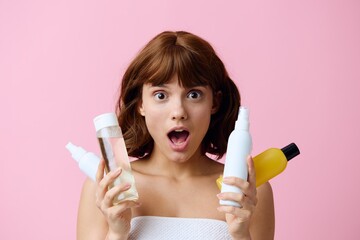 a close horizontal photo on a pink background of a shocked, surprised woman, holding various care products in her hands and looking at the camera with her mouth wide open. Skin care topics