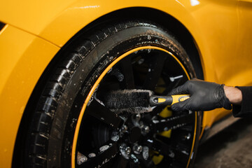 Auto wash service. Cropped close up image of male hands in black protective gloves, cleaning alloy...