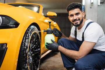 Washing a car in detailing service. Indoor shot of male worker in overalls, washing the car wheels...