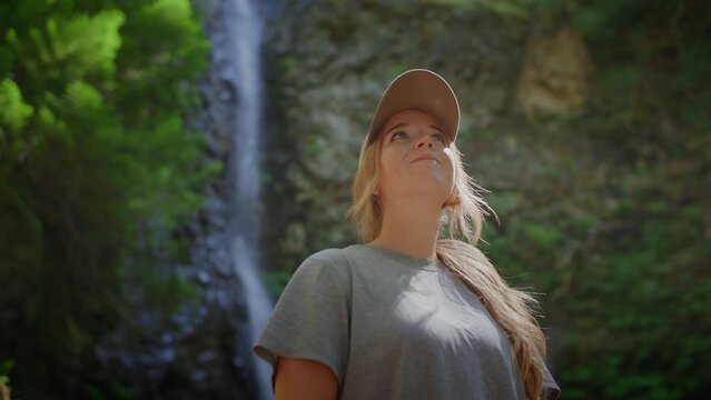 Low angle of woman looking around in forest, waterfall in background