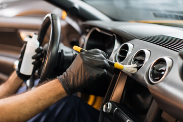 Cropped image of hands of young male worker in black protective gloves, cleaning car dashboard with...