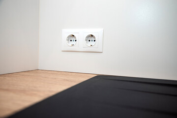 Two white european electrical sockets on a white smooth wall, front view, selective focus