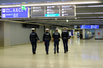 four young policemen in uniform, with weapons, walk around hall of Frankfurt am Main Airport in...