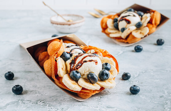 Delicious bubble waffle with ice cream, banana and blueberry on gray marble background.