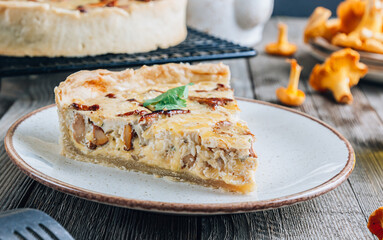 Homemade quiche or tart with chanterelles on rustic wooden background.