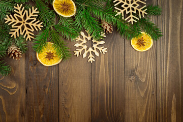 Christmas background with spruce branches, wooden snowflakes, cones, slices of dried oranges and stars of anise on a brown board. Copy space. Flat lay.