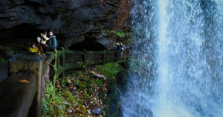 family, tourists are walking behind the Dry Falls waterfall, tourist attraction in Nantahala National Forest, North Carolina. A trail behind the natural waterfall in Appalachian mountains