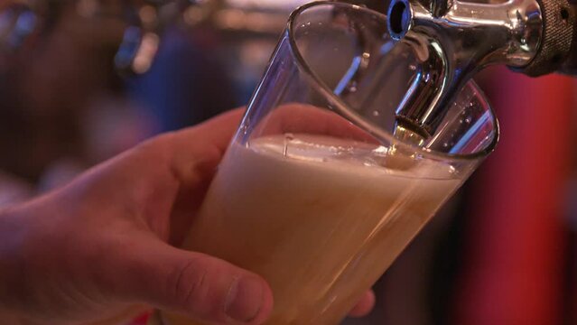 draft beer being poured into a clear glass using a metal draft keg in a dark and busy bar 