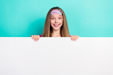 Photo of adorable excited school girl rising huge white blank board empty space smiling isolated teal color background