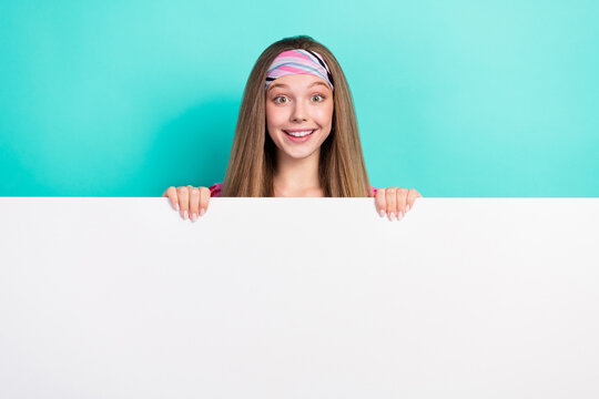 Photo of adorable excited school girl rising huge white blank board empty space smiling isolated teal color background - Powered by Adobe