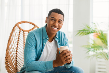 Cheerful young african american man with coffee cup takeaway enjoy drink and calm in light living...