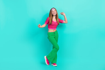 Ganzkörperfoto eines charmanten, verträumten Schulmädchens in pinkfarbener, bauchfreier Hose, die tanzt und Spaß hat, isolierter blaugrüner Hintergrund