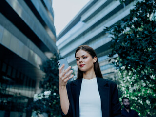 Business woman brunette portrait with phone in hand in business jacket in the city of multistory office buildings, the concept of business competition in the city