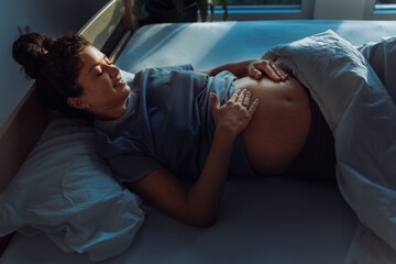 Pregnant woman laying in bed and looking at belly