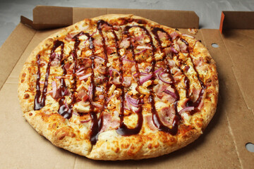Round ready-made fresh pizza with dark sauce chicken with barbecue sauce lies in the box side view. Food fast delivery