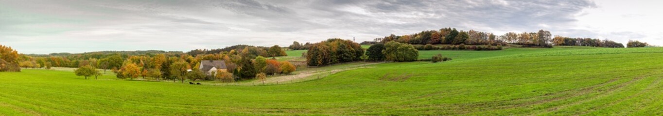 Fototapeta na wymiar Panoramic rural autumn landscape in North Rhine Westphalia in Germany. Farm house in the middle of a huge green field.