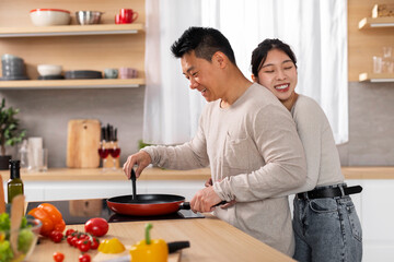 Fototapeta na wymiar Loving asian woman hugging her boyfriend cooking meal