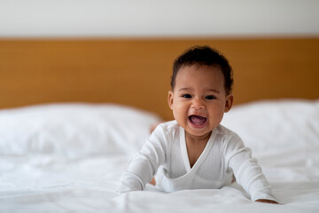 Adorable Little African American Baby Wearing Bodysuit Crawling On Bed At Home