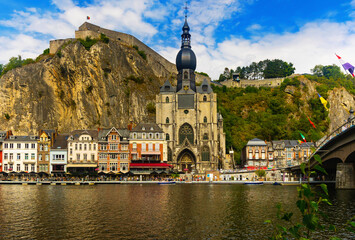 Fototapeta na wymiar View of residential buildings, Notre Dame de Dinant church and citadel on cliff from riverbank of Meuse River. Dinant, Waloon Belgium.
