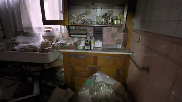 A personal perspective (POV) walking through a creepy abandoned home's kitchen and dining room. Wallpaper peeling off and junk all over the floor. Flashlight shows the way.  	