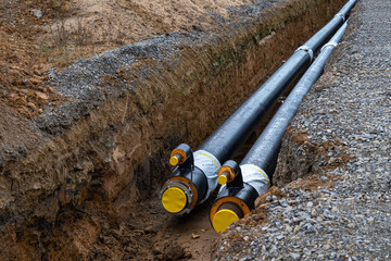 Large black metal pipes with a plastic sheath laid in a trench. Modern pipeline.