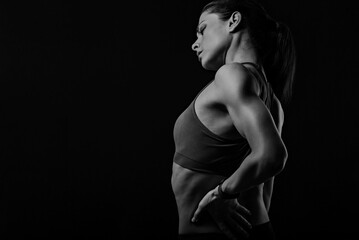 Sporty woman holding hands to relax the tension and pain in lower back and sacrum in sport top on empty copy space studio background. Back view. The concept of medicine. - obrazy, fototapety, plakaty