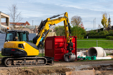 Yellow excavator and red metal container at the construction site.