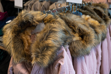 Winter jackets with fur collars hanging on plastic hangers in a store.