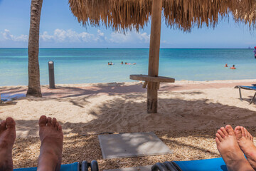 View of feet of man and woman on sunbeds on sandy beach.  Gorgeous turquoise water surface of...