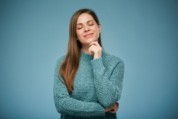 Smiling thinking woman with closed eyes in casual clothes touching her chin. Advertising female studio portrait on blue.