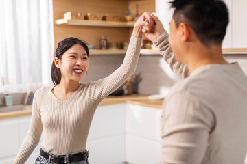 Happy korean spouses dancing waltz at kitchen