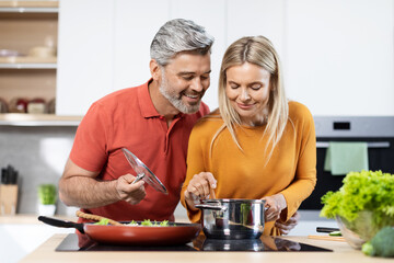 Beautiful middle aged man and woman cooking together at kitchen