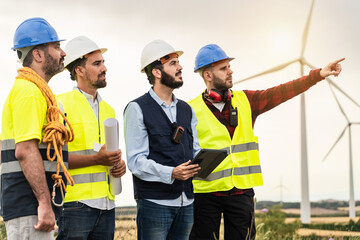 Professional workers working in front of windmill Electricity station. Back view of Civil Engineer and electricians discussing about projects