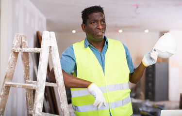 Portrait of disgruntled african american worker in yellow vest in a cottage under construction