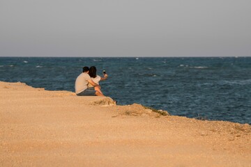 Selective focus shot of a couple sitting at the shore of the beach
