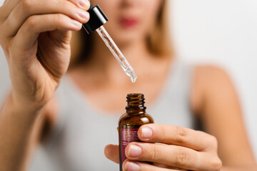 Face serum pipette close-up in hands of attractive girl on white background. Girl applies face...