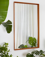 Vintage danish modern wooden teak frame mirror. Interior scene with white walls and large green house plants. 