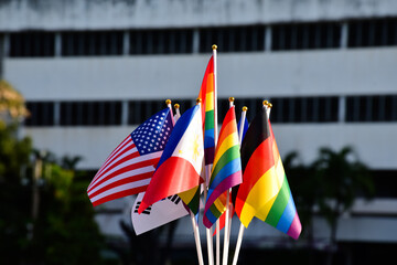 Rainbow flags and flags of many countries in front of big building of asian school, concept for celebration of lgbtq+ genders in pride month around the world, soft and selective focus.