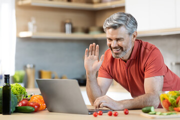 Cheerful man cooking at home, having video call, using laptop