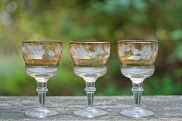 a row of white brown three glass crystal goblets on a gray wooden table outdoors on a green background